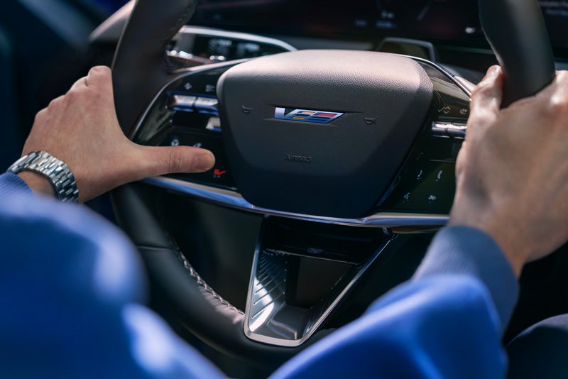 Close-up of a Man About to Press the V-Button on the 2026 OPTIQ-V Steering Wheel | Ghent Cadillac in Greeley CO